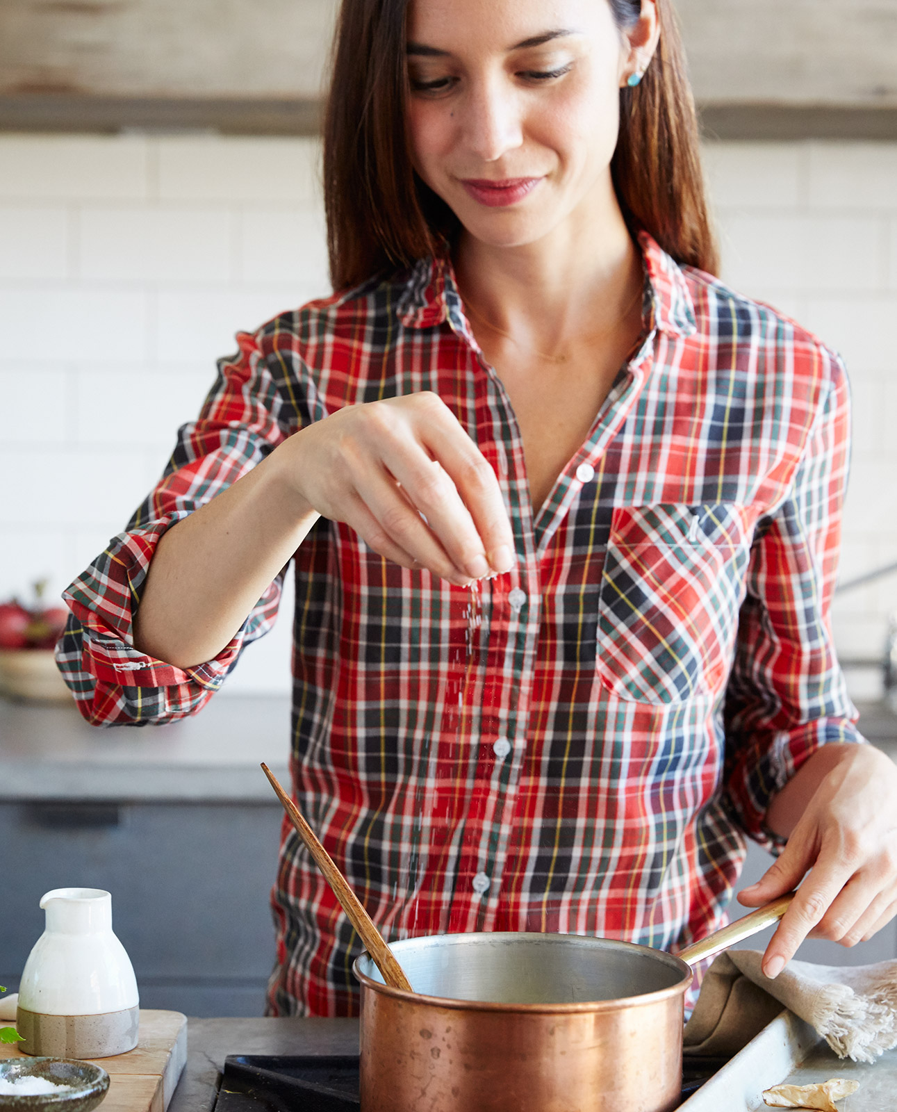 woman seasoning pot of soup in kitchen