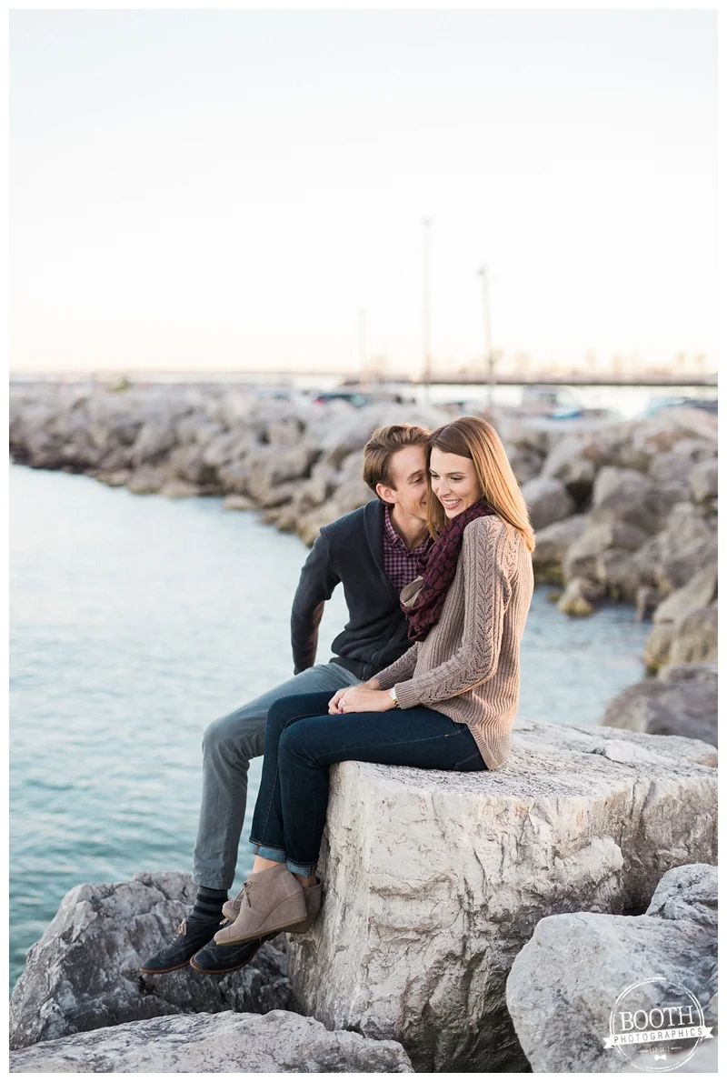 engaged couple sitting along the rocks on Lake Michigan n Milwaukee Wisconsin