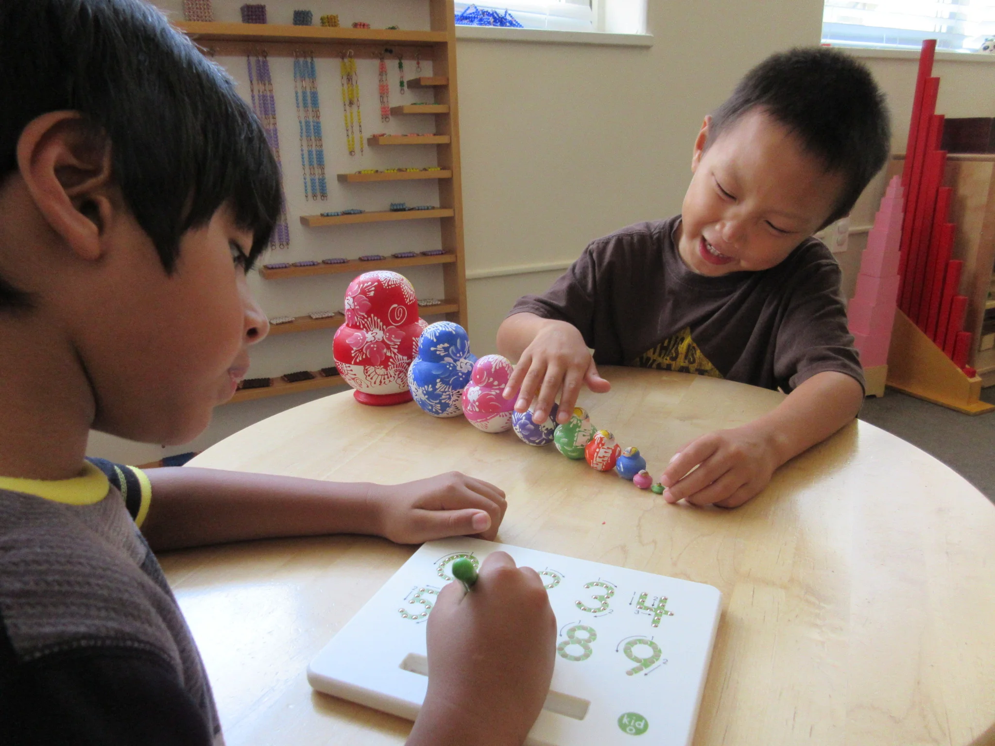 One child uses a magnetic number tracing board while his friend works with a set of nesting dolls.
