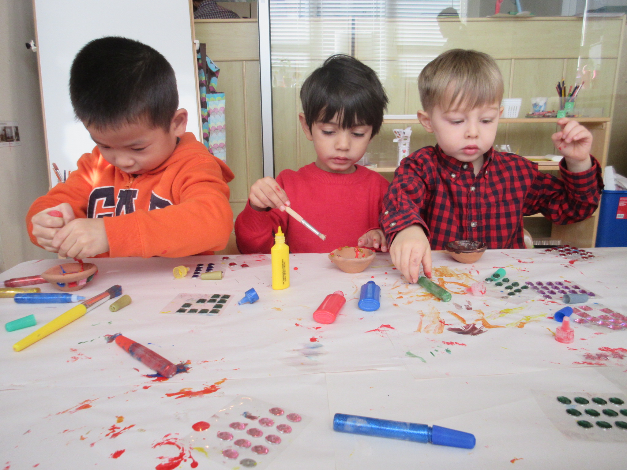 Three friends sit together and decorate their candle holders.
