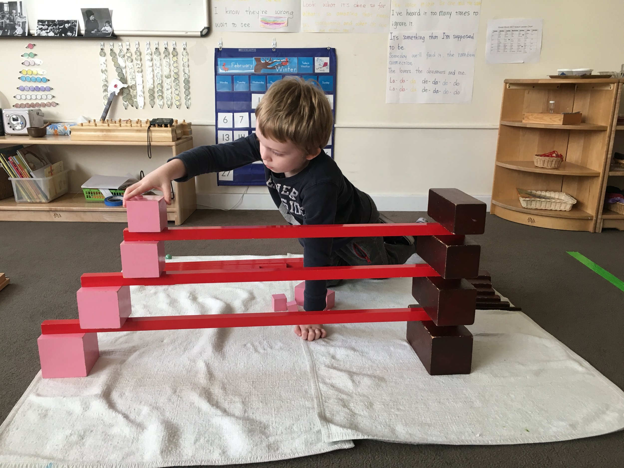 A child creates a pattern using three Sensorial works.