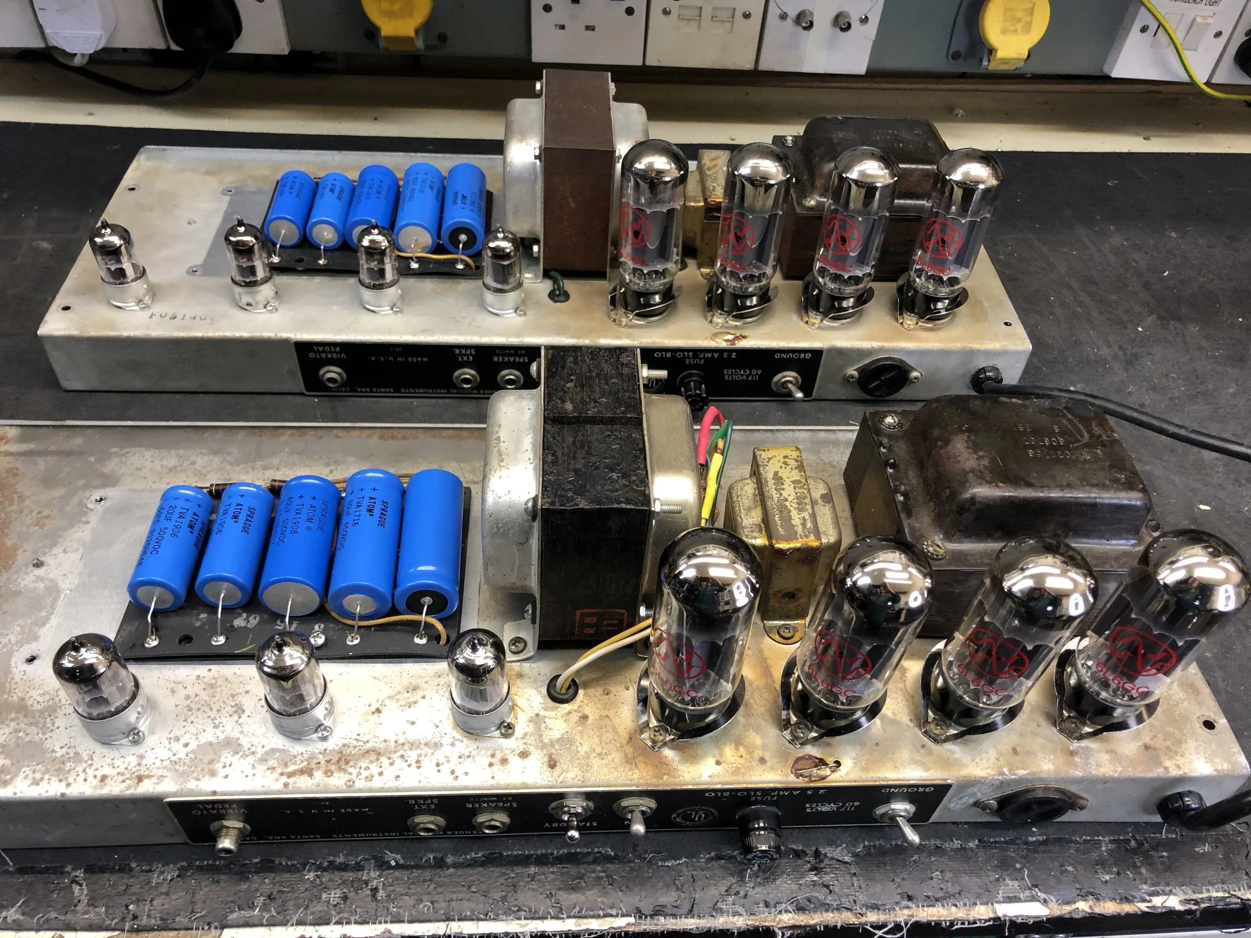 Close-up of a vintage vacuum tube amplifier with glass tubes and blue capacitors mounted on a metal chassis.
