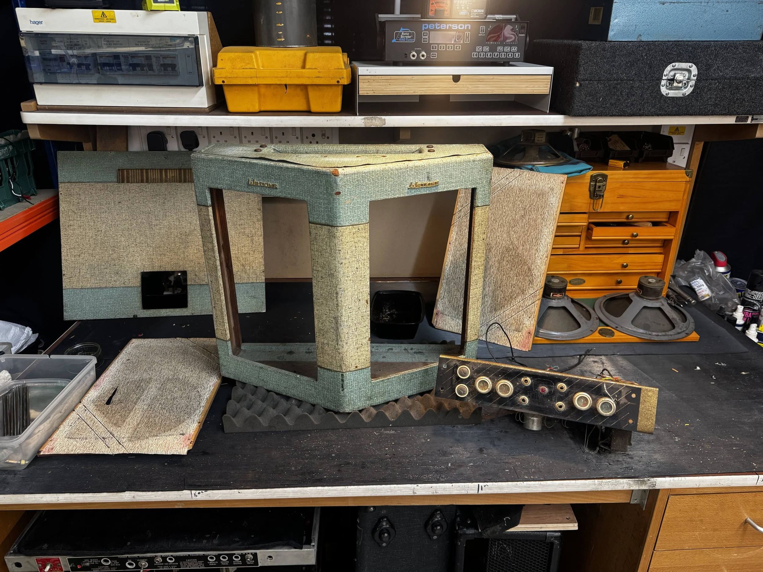 A workbench with various vintage audio equipment, including speakers, amplifiers, and audio accessories, arranged on and underneath the table.