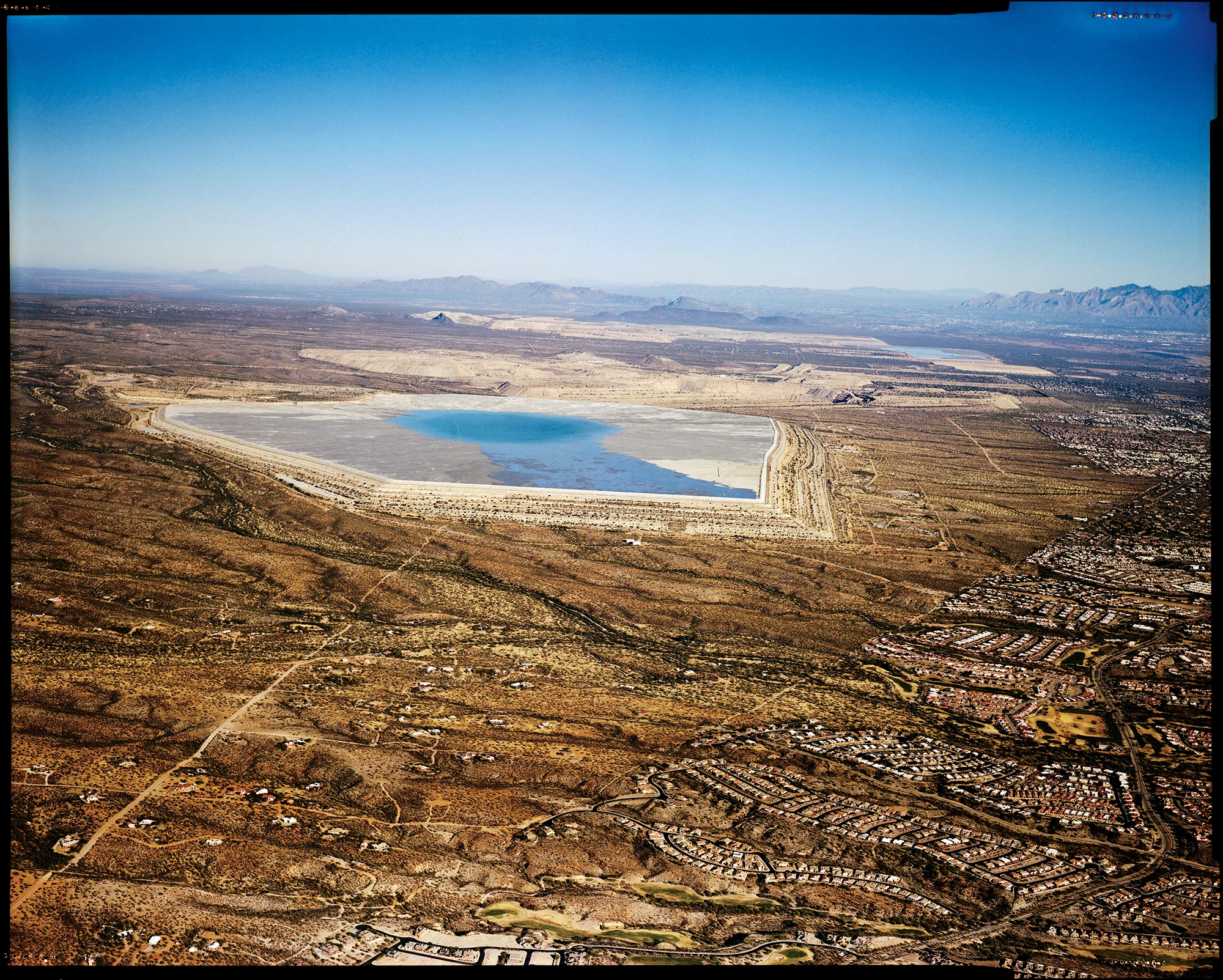 A tailings pond of waste materials left over after the copper-ore extraction process at the Sierrita Mine, near the Canoa Estates retirement community (center right). Copper mines, along with golf courses are significant contributors to water depletion in Arizona, which has been in a drought for over two decades.