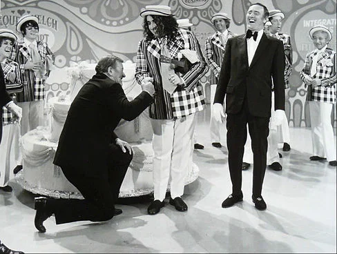 John Wayne and Tiny Tim helped Laugh-In celebrate its 100th episode in 1971. Co-host Dan Rowan yucks it up in his tuxedo .