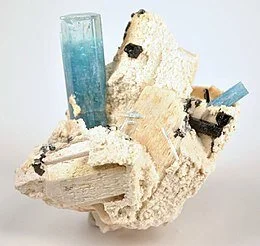Perched on crystallized, white feldspar is an upright  aquamarine crystal.