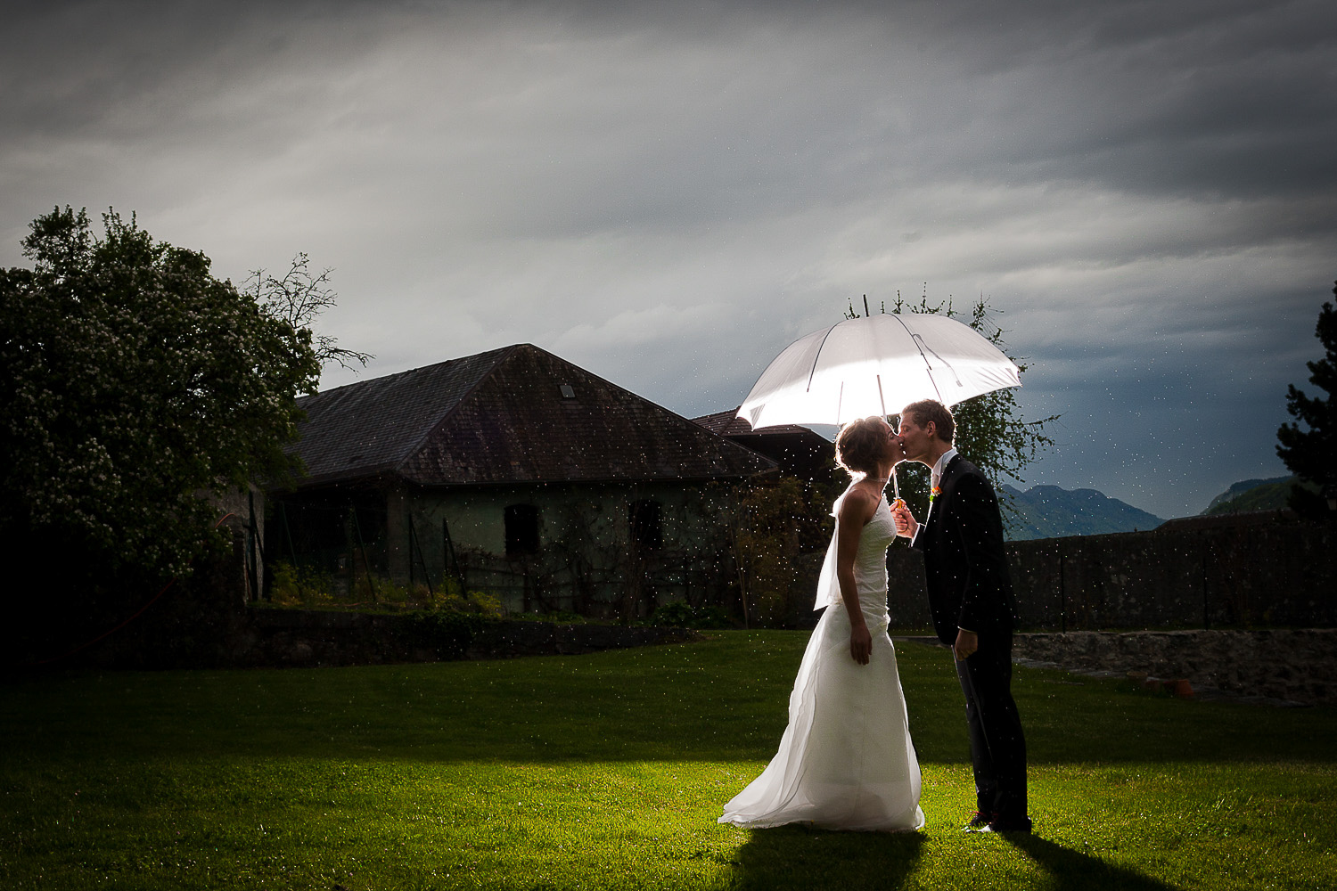 Baiser jeunes mariés sous parapluie, Annecy, Photographer mariage Lausanne
