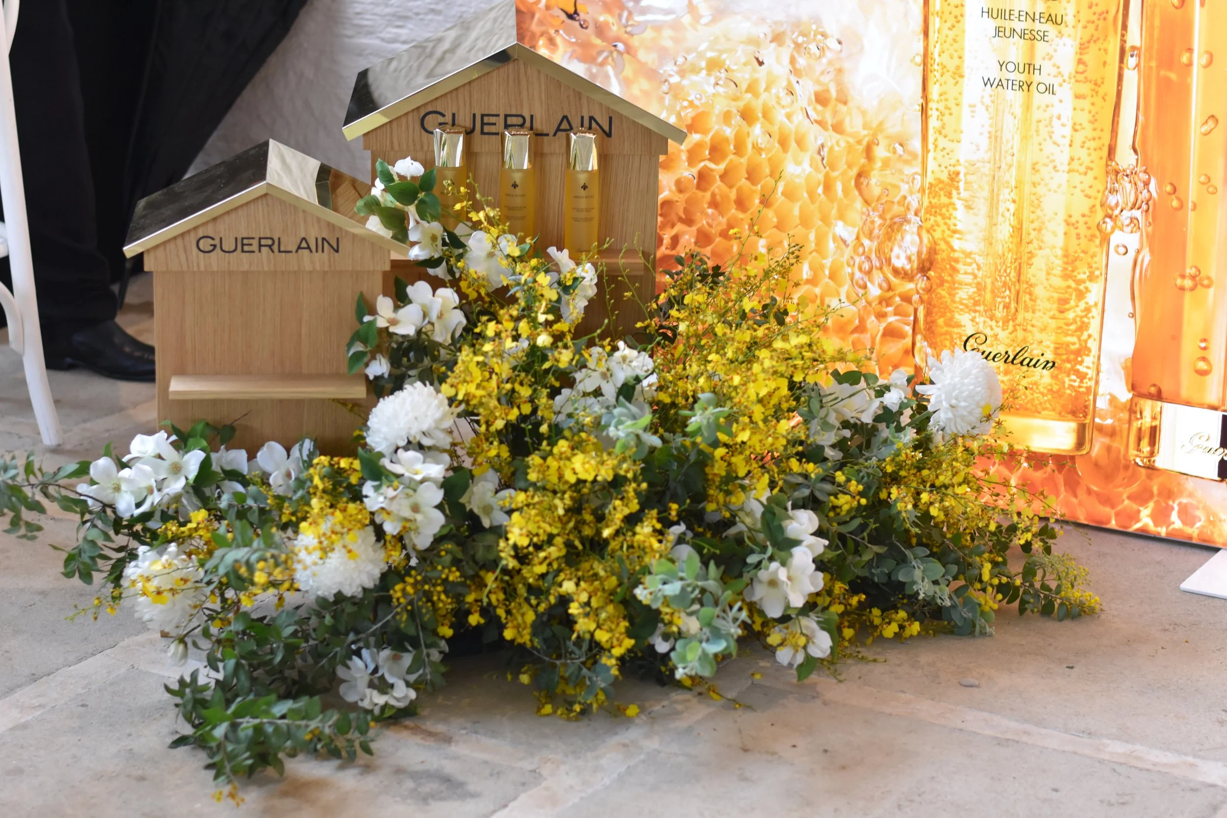 Display of Guerlain beauty products with floral arrangement and golden perfume bottles.