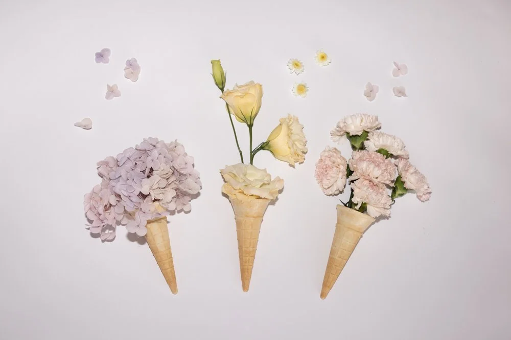 Bride in lace wedding dress holding a bouquet of white roses, hydrangeas, and greenery near a window.