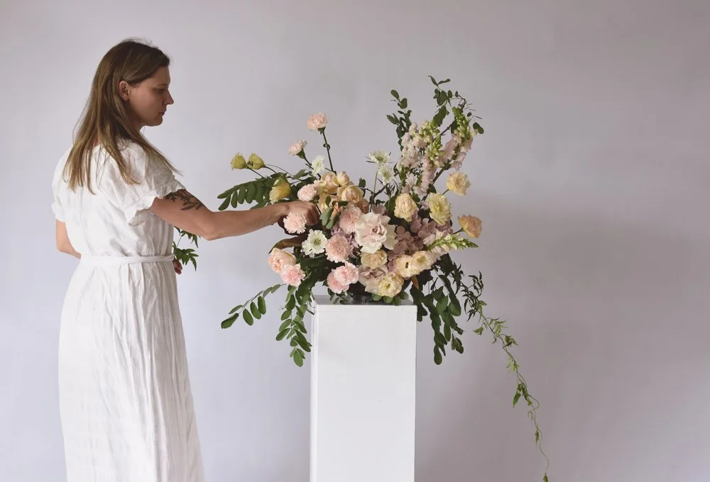 Woman arranging a floral centerpiece on a long dining table decorated for a special event.