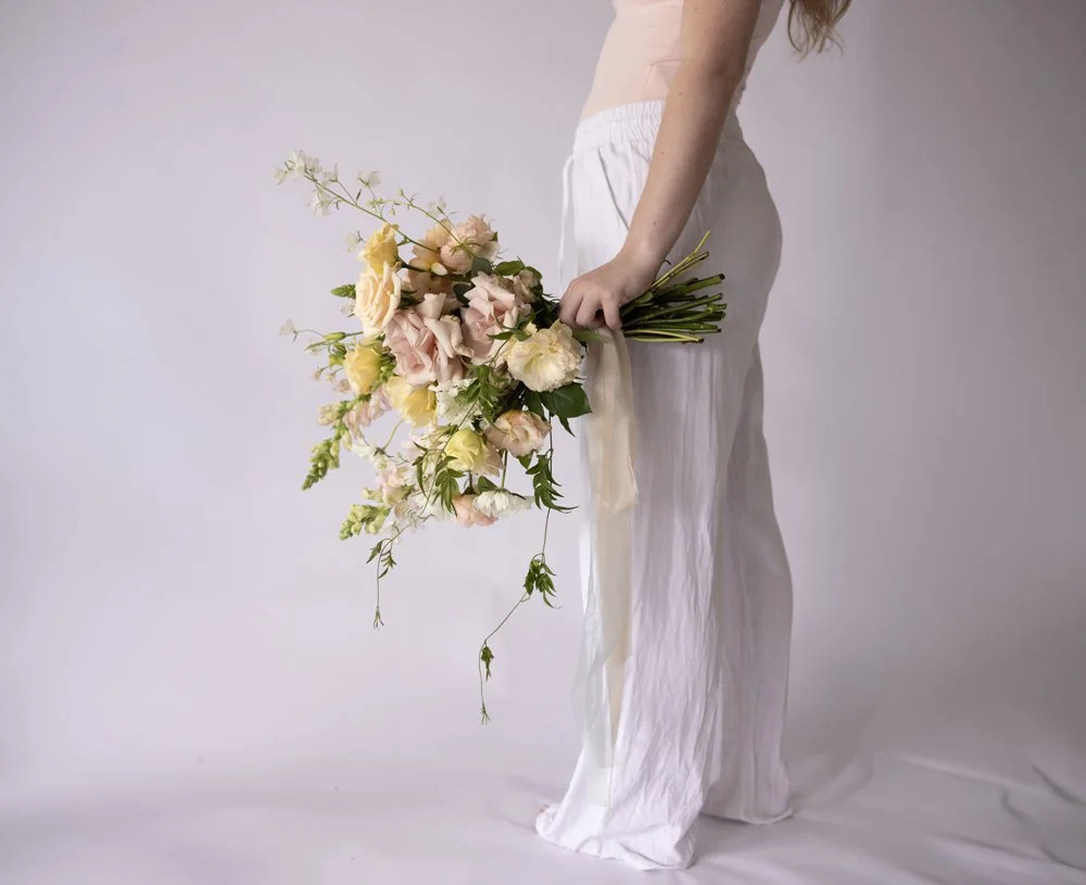 Various pastel-colored flower bouquets, including roses, orchids, and other flowers, arranged in clear glass vases on a white fabric background.