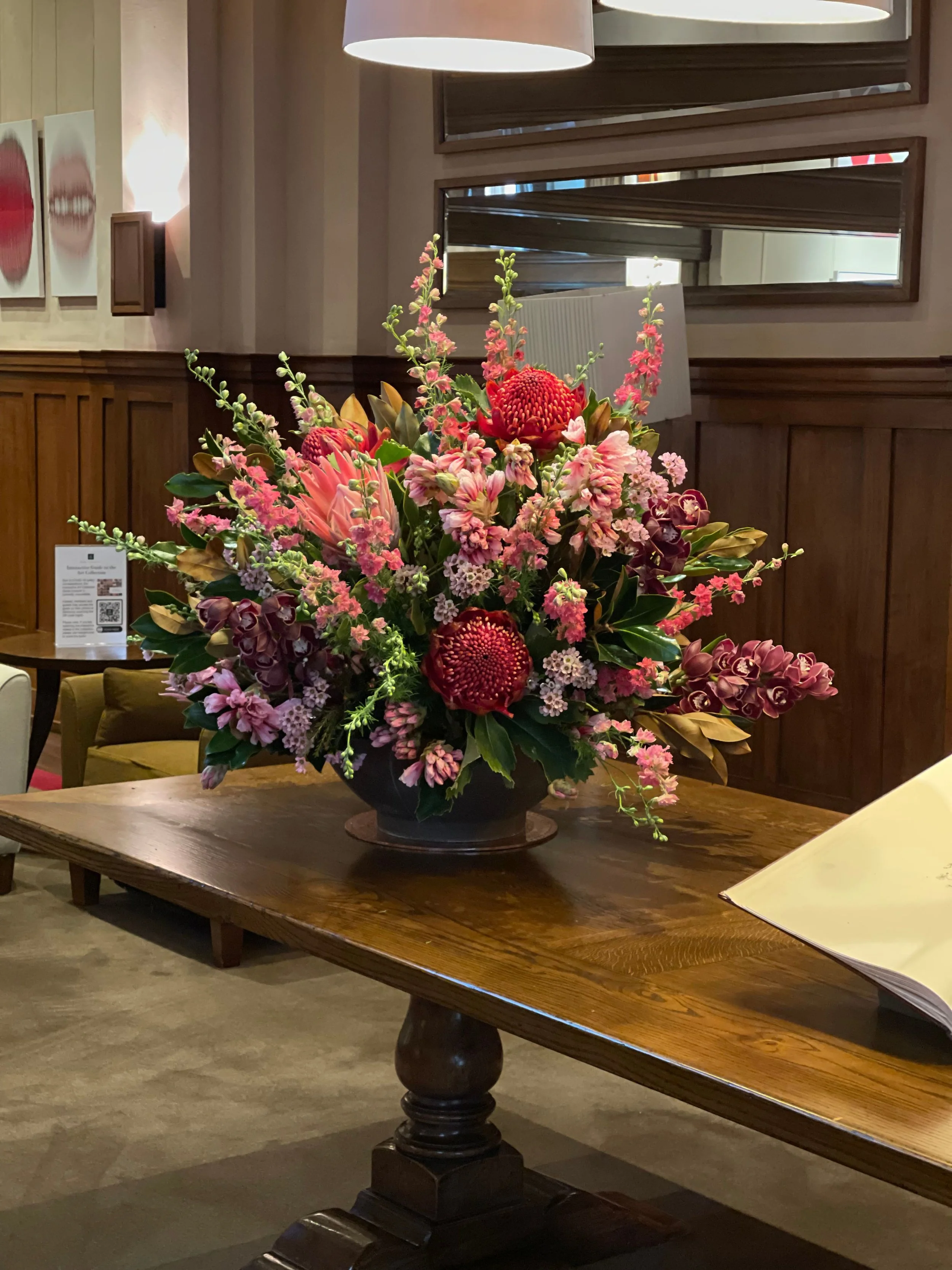 A large pink and red floral arrangement on a wooden table in an indoor setting.