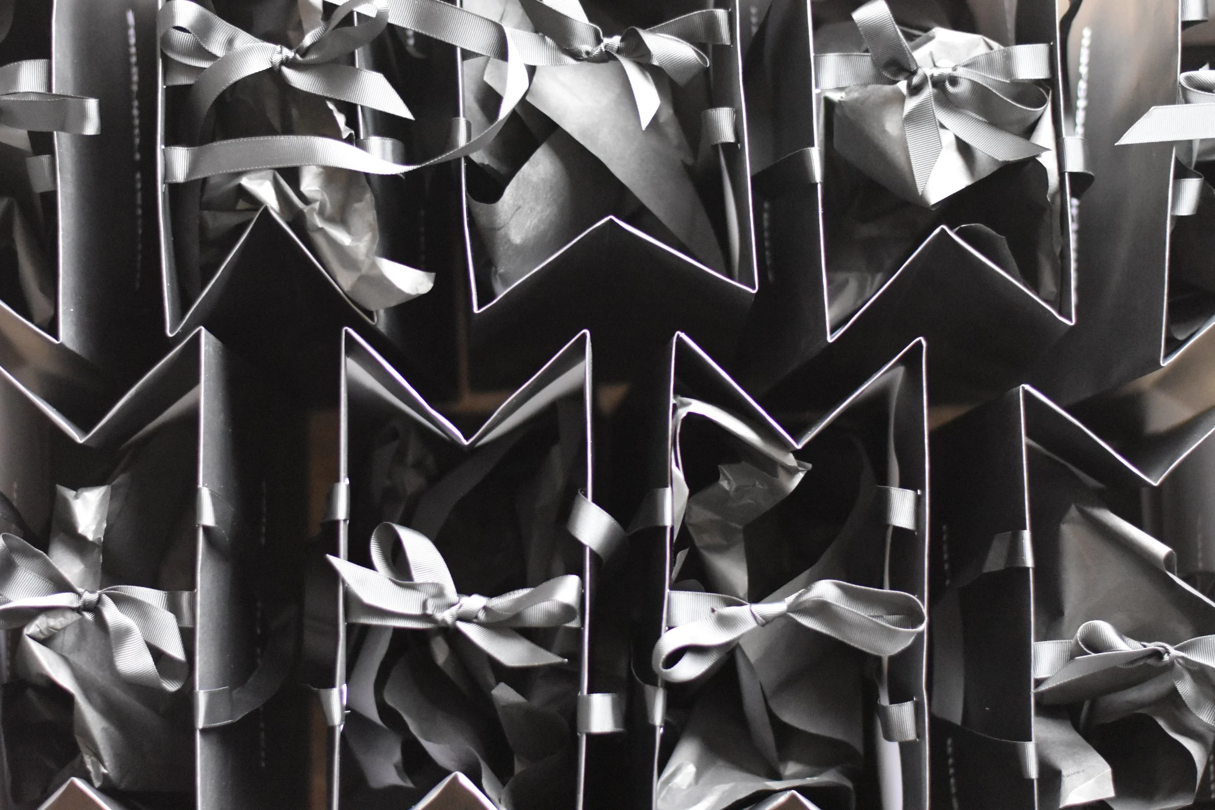 Black gift bags with silver ribbons arranged in a grid on a display rack.