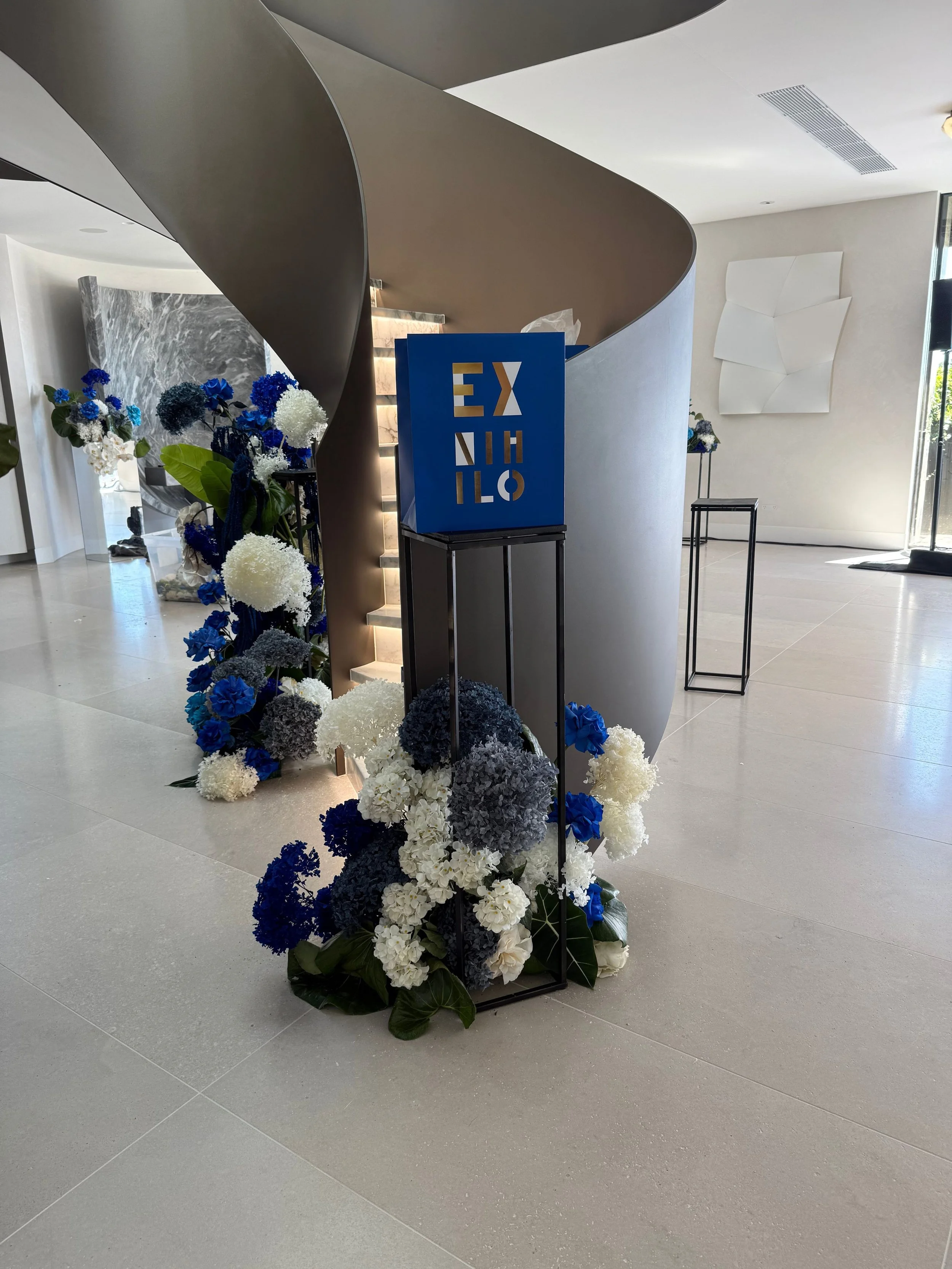 Contemporary lobby with modern spiral staircase, floral arrangement with white, blue, and gray hydrangeas, and abstract artwork on the wall.
