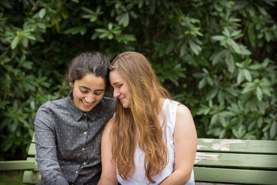  Couple sitting on a green bench outside smiling and looking down. 