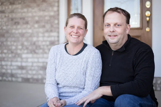Couple smiling at camera and sitting on a front porch.