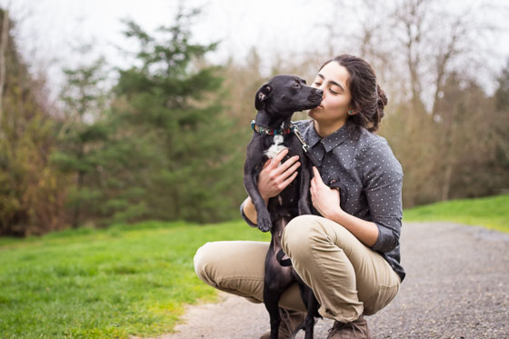 Person holding and kissing cute black puppy in a park.