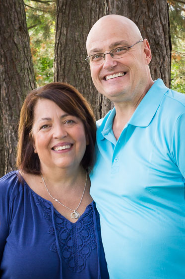  Couple in blue shirts smiling in front of trees. 