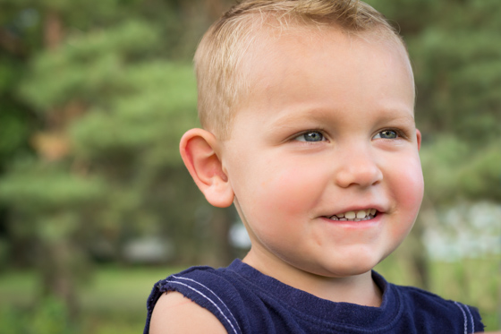  Close up of small child in blue shirt outside looking off camera. 