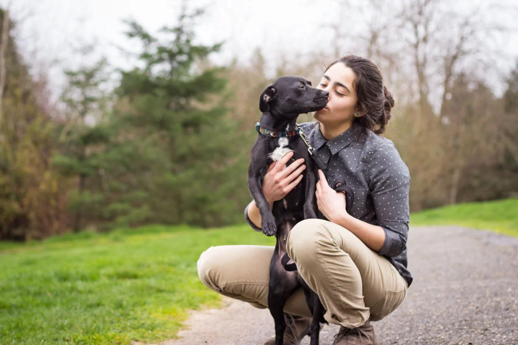 Person kissing black puppy dog in a park.
