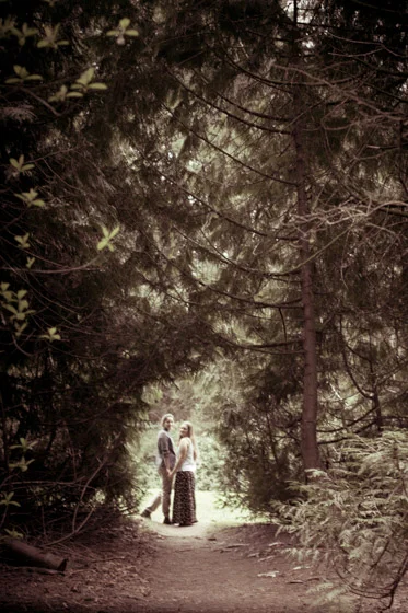 Couple in distance holding hands in the light seen through a tunnel of trees.