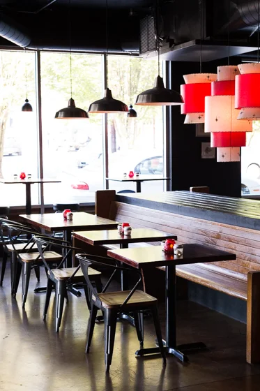 Darkly lit restaurant with iron and wood furniture and red lamps
