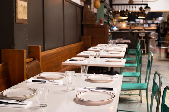 Softly lit dining area with white tables, wood booths, and turquoise metal chairs