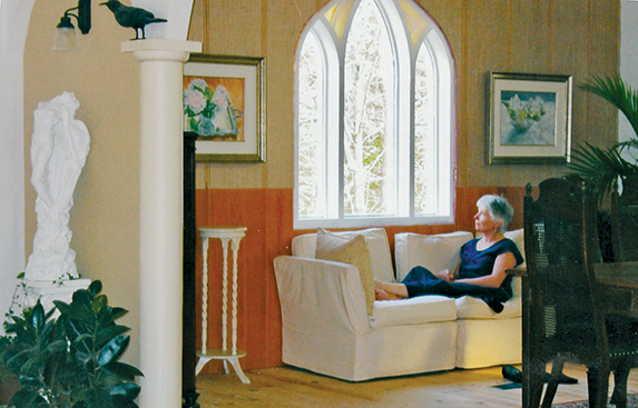 Now finished, the stained glass window becomes a showcase over a relaxing nook. Nancy Woodall shown here is enjoying the benefits of Patrick Nash’s decision to move the window. Photo courtesy Nancy Woodall.