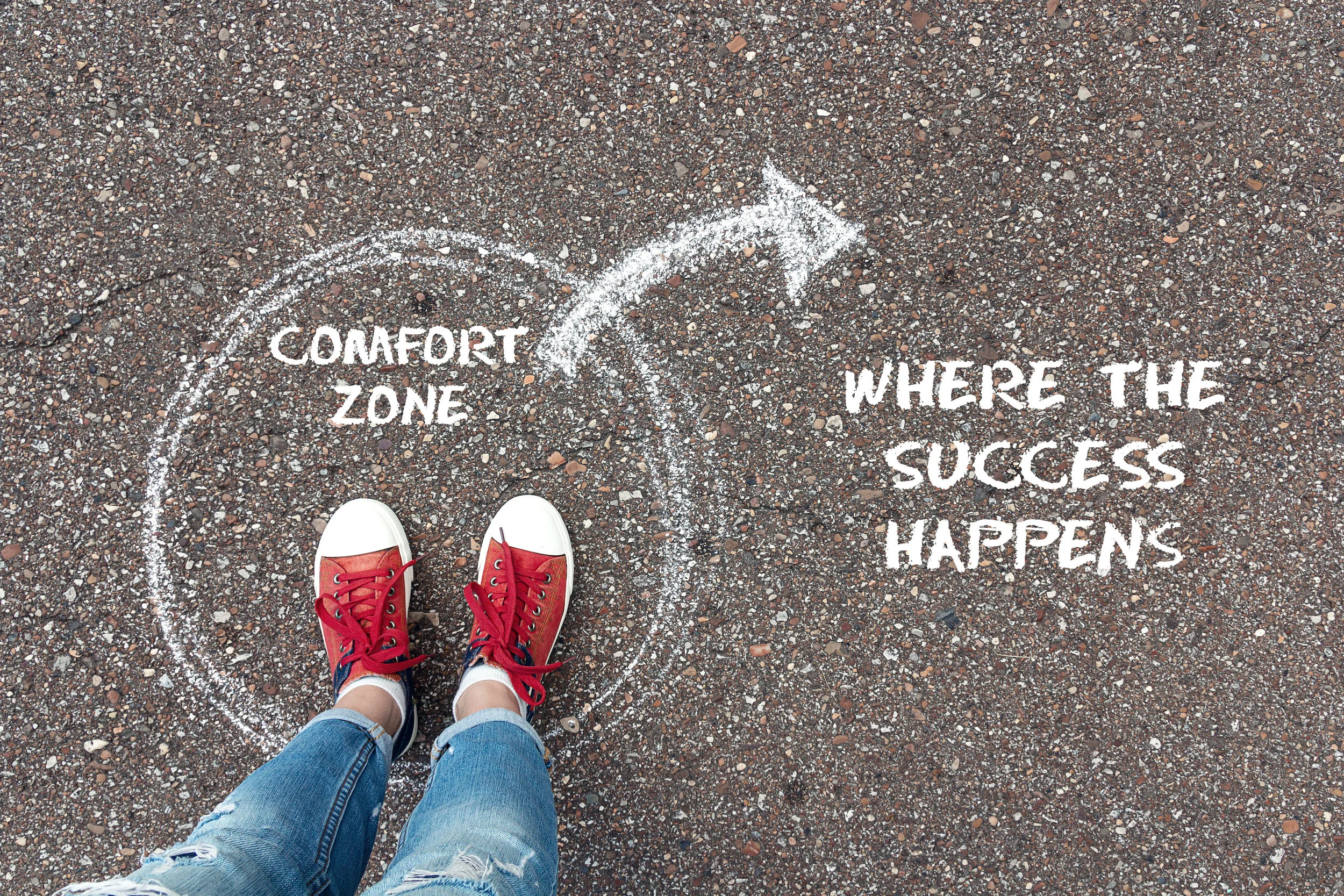 Exit from the comfort zone concept. Feet standing inside circle comfort zone and outward arrow chalky on the asphalt.