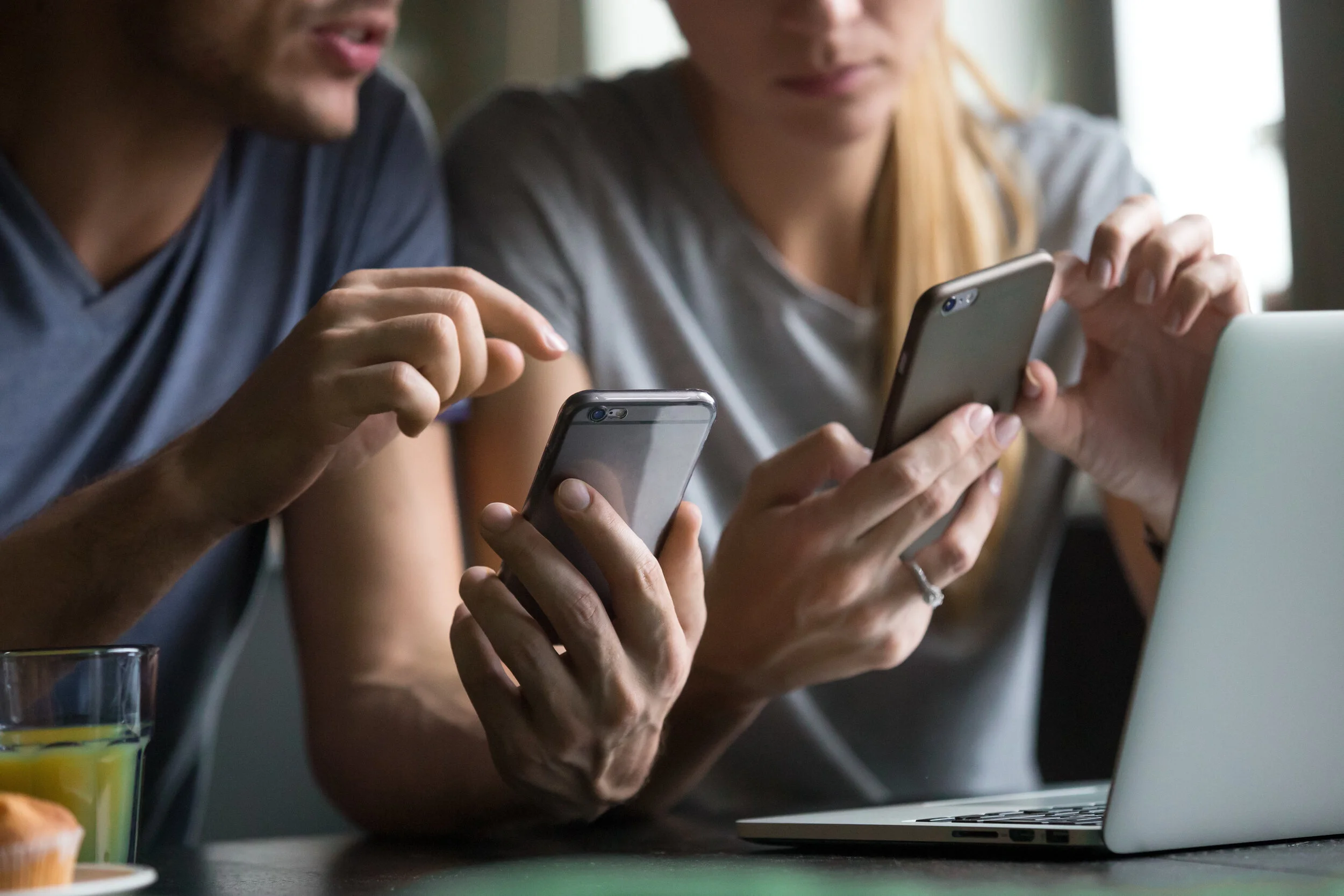Close up view of man and woman using smartphones discussing mobile apps concept, couple talking holding cellphones synchronizing information online with laptop, checking news or texting messages