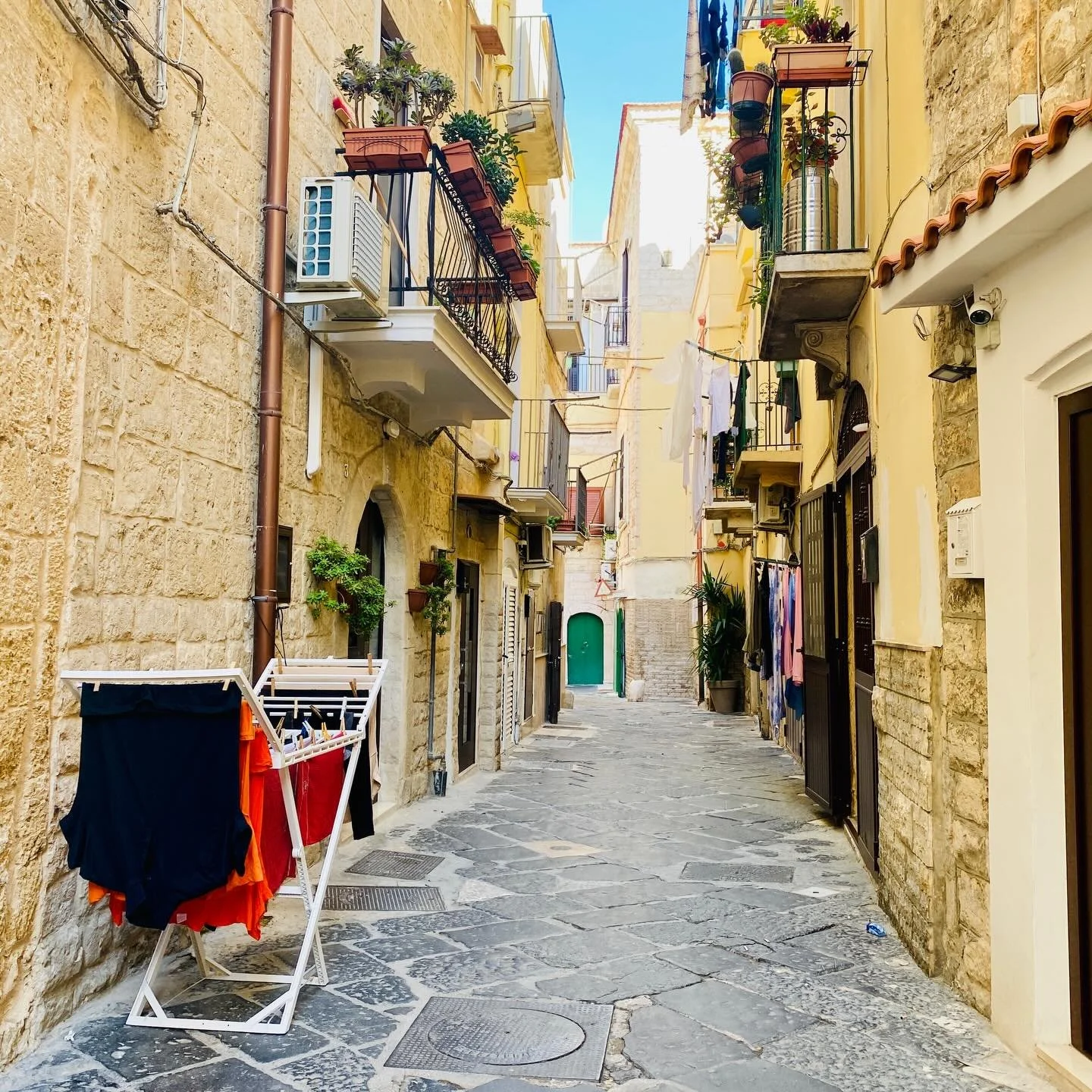 Bari doesn&rsquo;t hide everyday life indoors.
Curtains instead of doors means the intimacy of daily routines spills onto the street. You hear the chime of forks on plates, a TV on in the background. Laundry hangs on a rack in the road. The whine of 