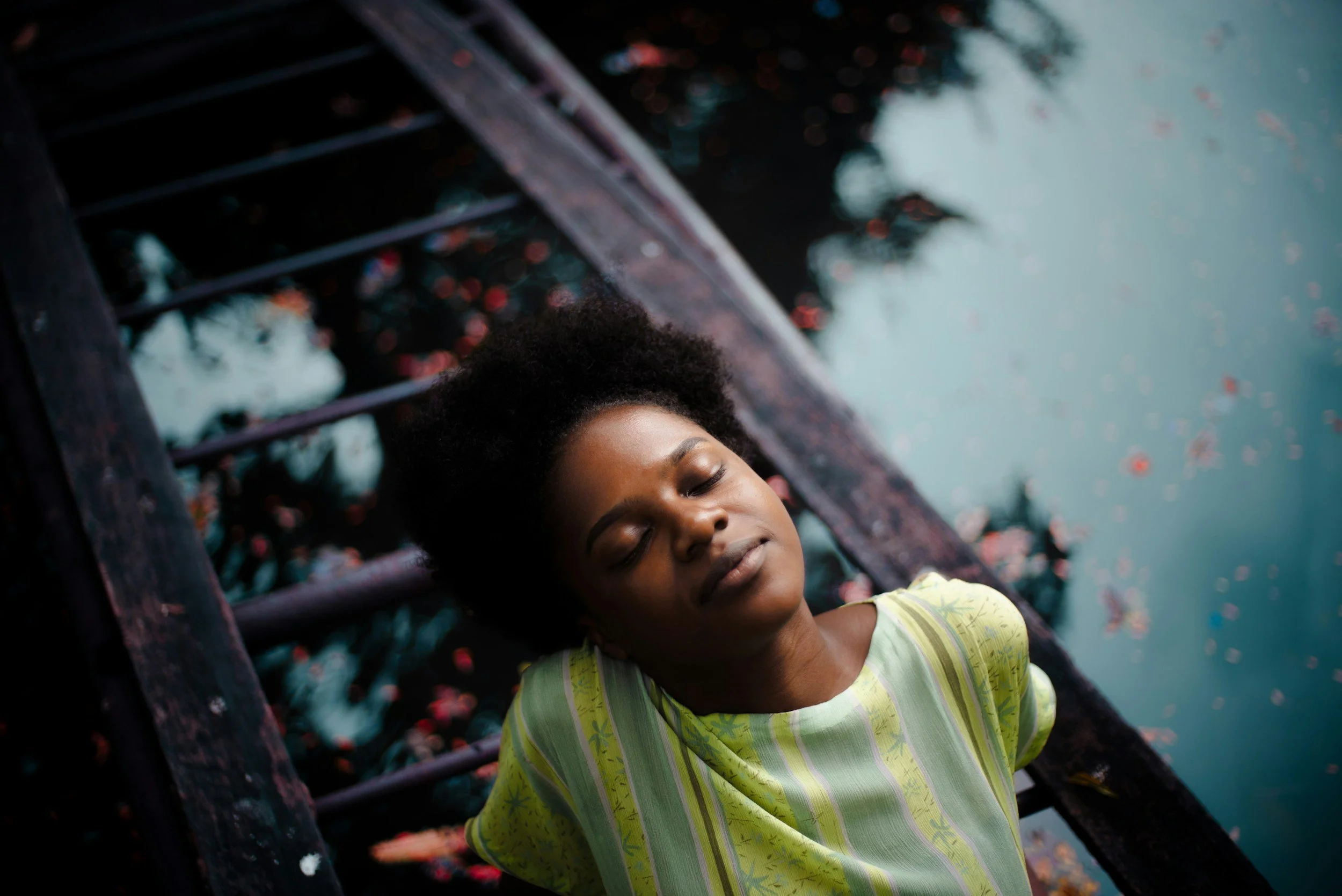A Black woman rests with her eyes closed in nature.