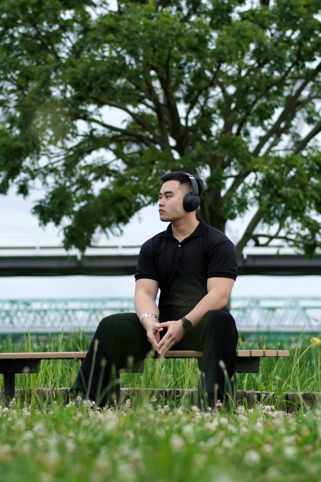 An Asian man wearing headphones sits on a bench outdoors, resting and creating boundaries.