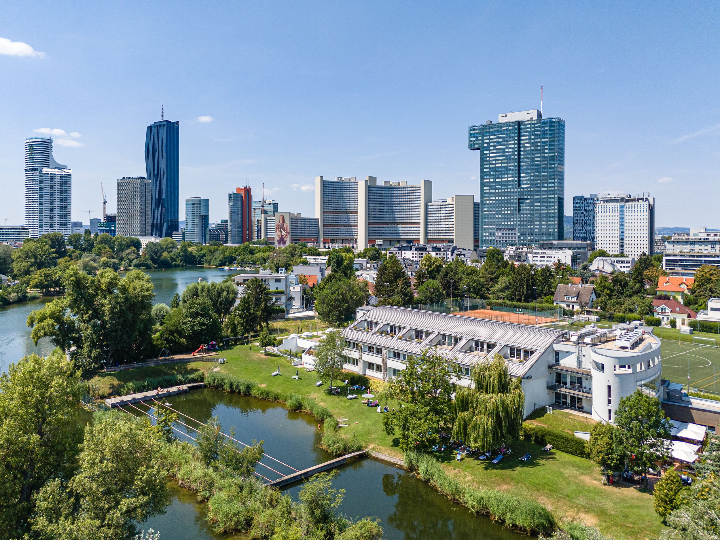 Skyline of Vienna with modern skyscrapers, a river, greenery, and urban buildings on a sunny day.