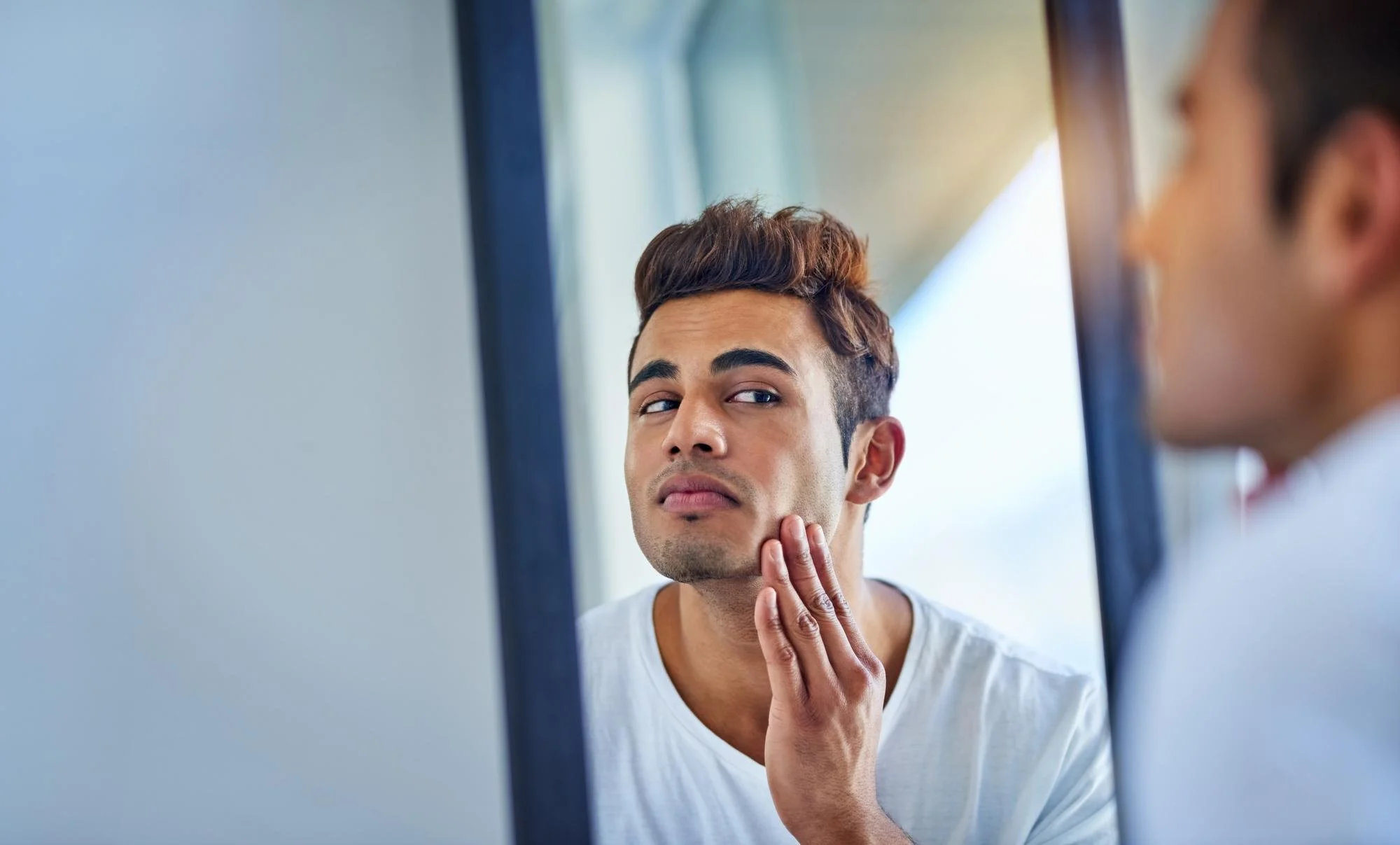 A man examining his skin in the mirror while healing, illustrating concerns about sun exposure after a chemical peel during recovery.