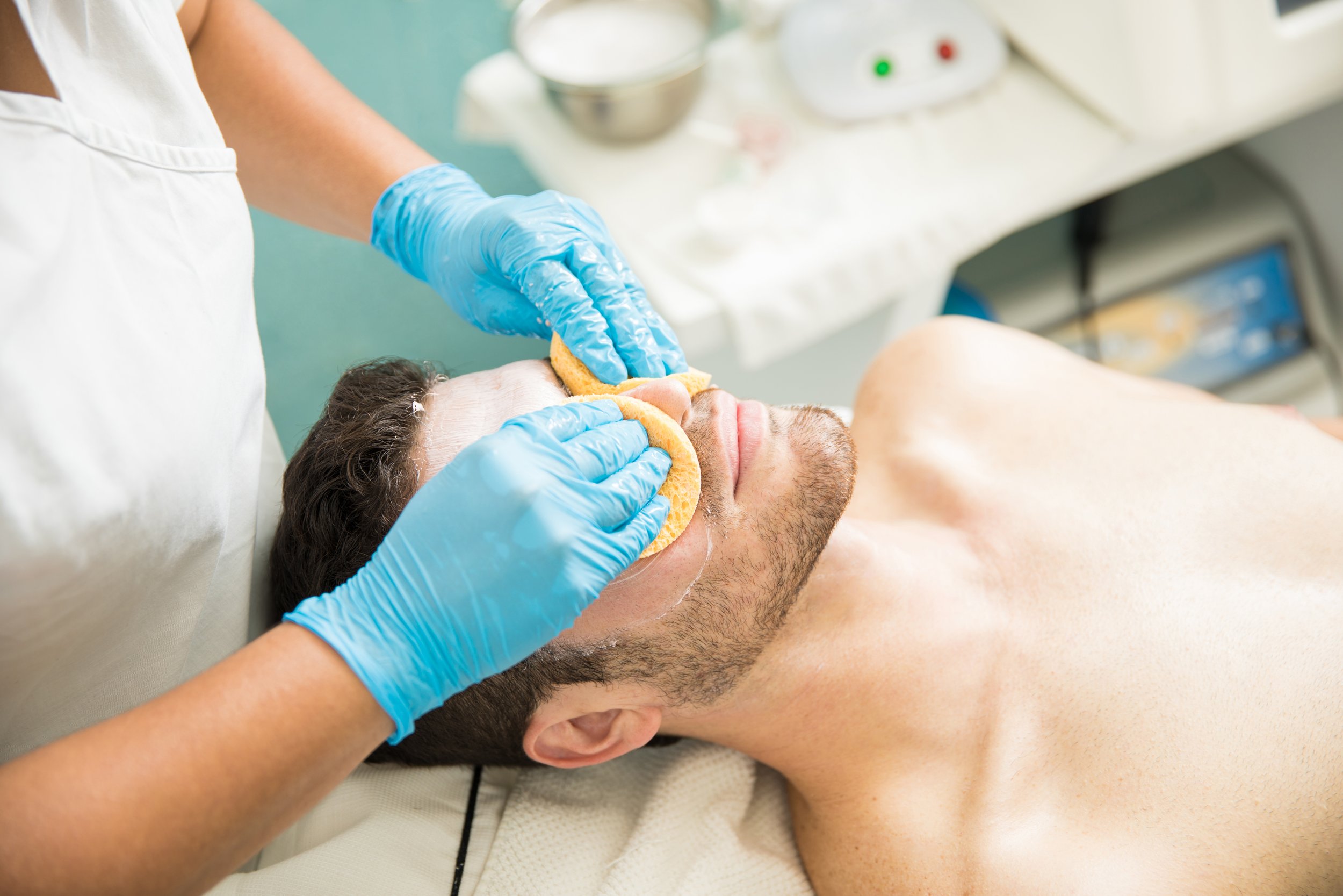 Therapist performing a professional facial cleanse on a young man during a spa visit.
