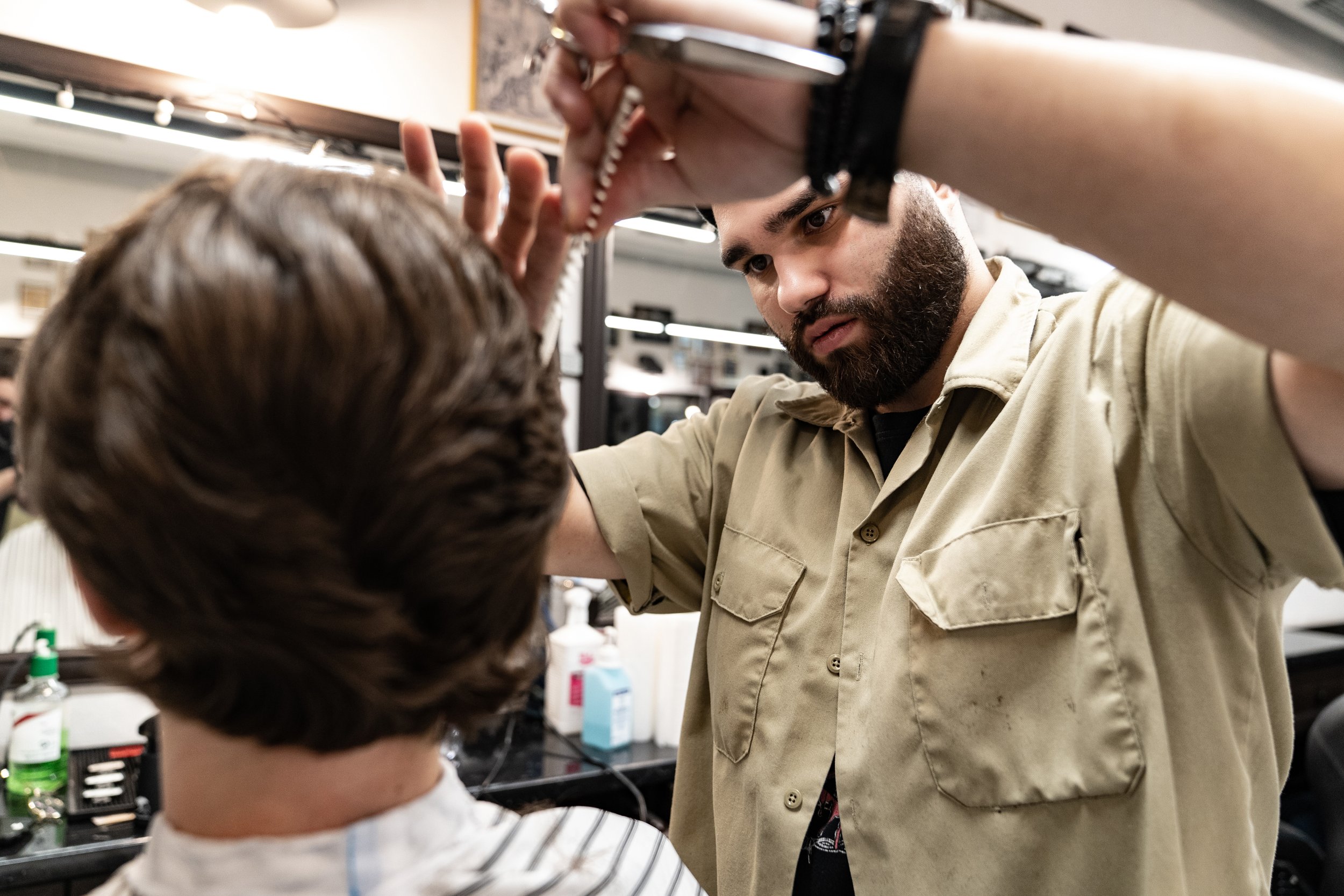 A barber combs up a section of hair and trims it with scissors during a men's haircut in Chicago.