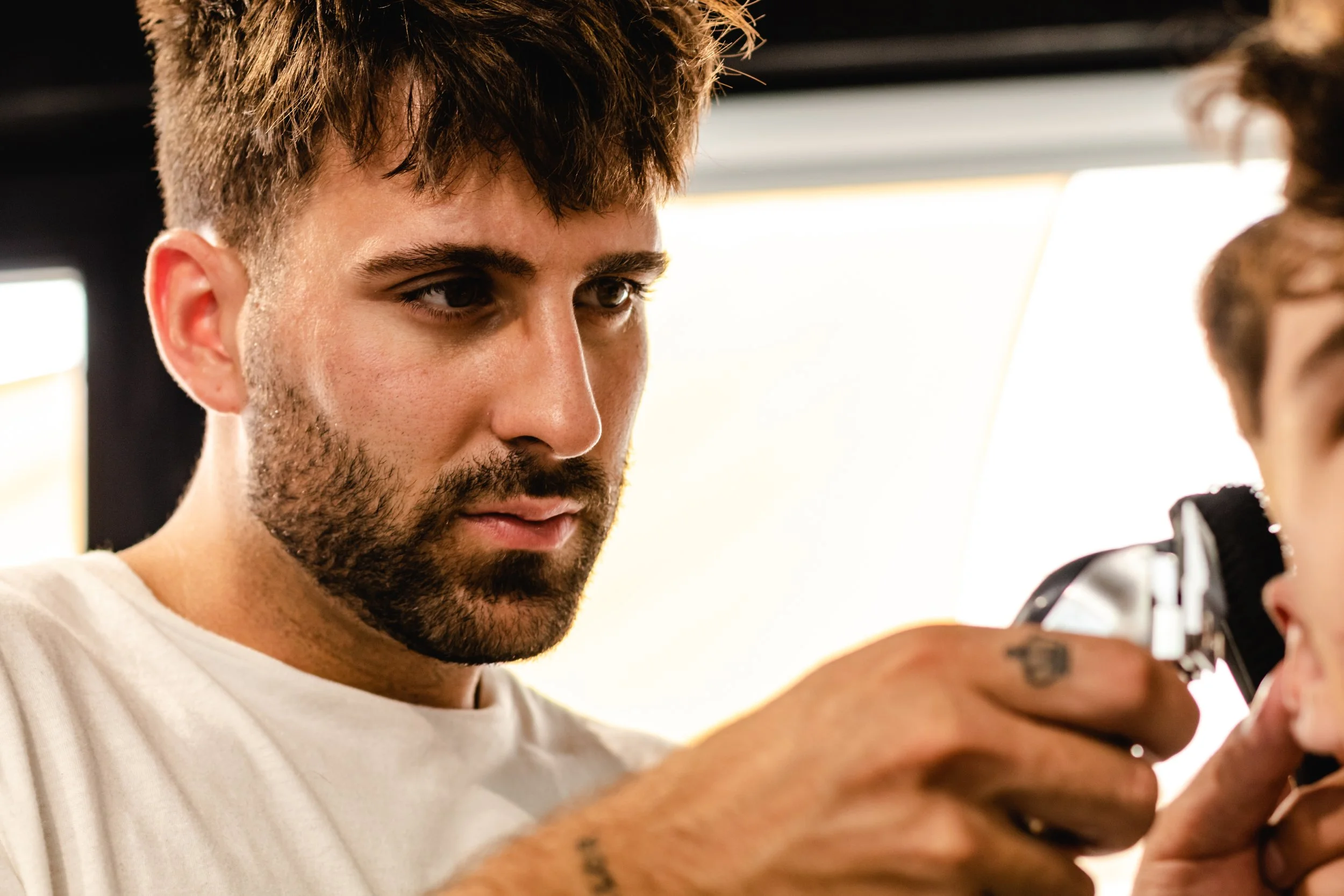 Barber using clippers to refine a fade haircut on a male client at a men's salon.