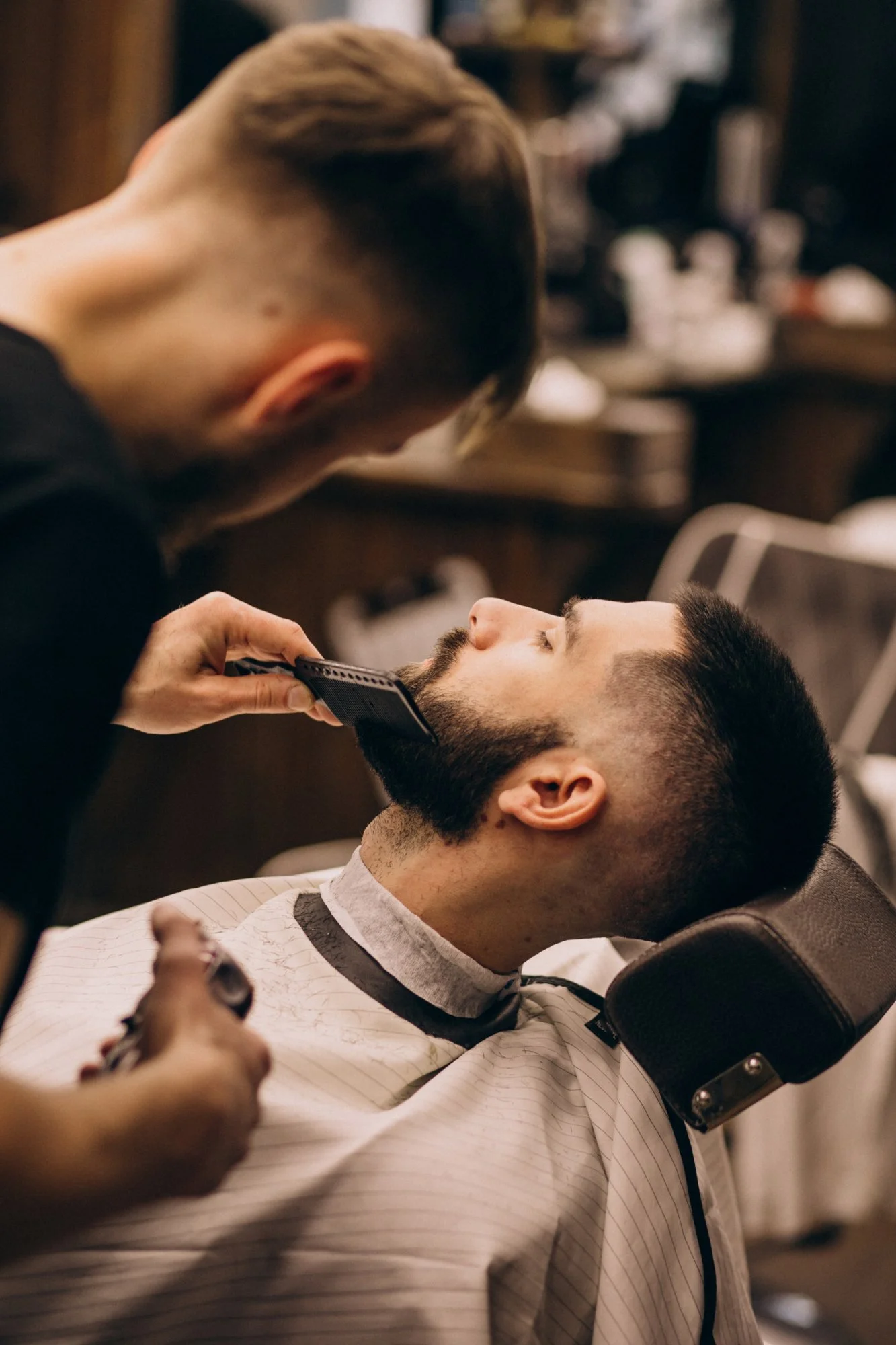 Stylist using an electric trimmer to shape a client's beard during a beard grooming appointment.