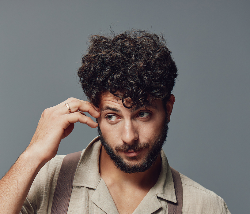 Man with long natural curly perm outdoors showing the kind of textured wave results available at a men's perm Chicago salon.