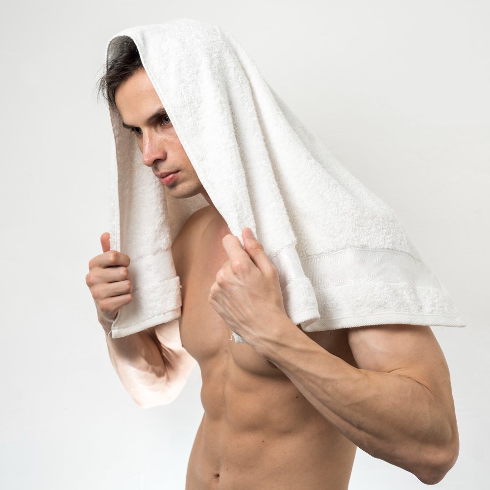 Confident man with a towel wrapped around his head, posing after a grooming session, portraying relaxed male self-care habits.