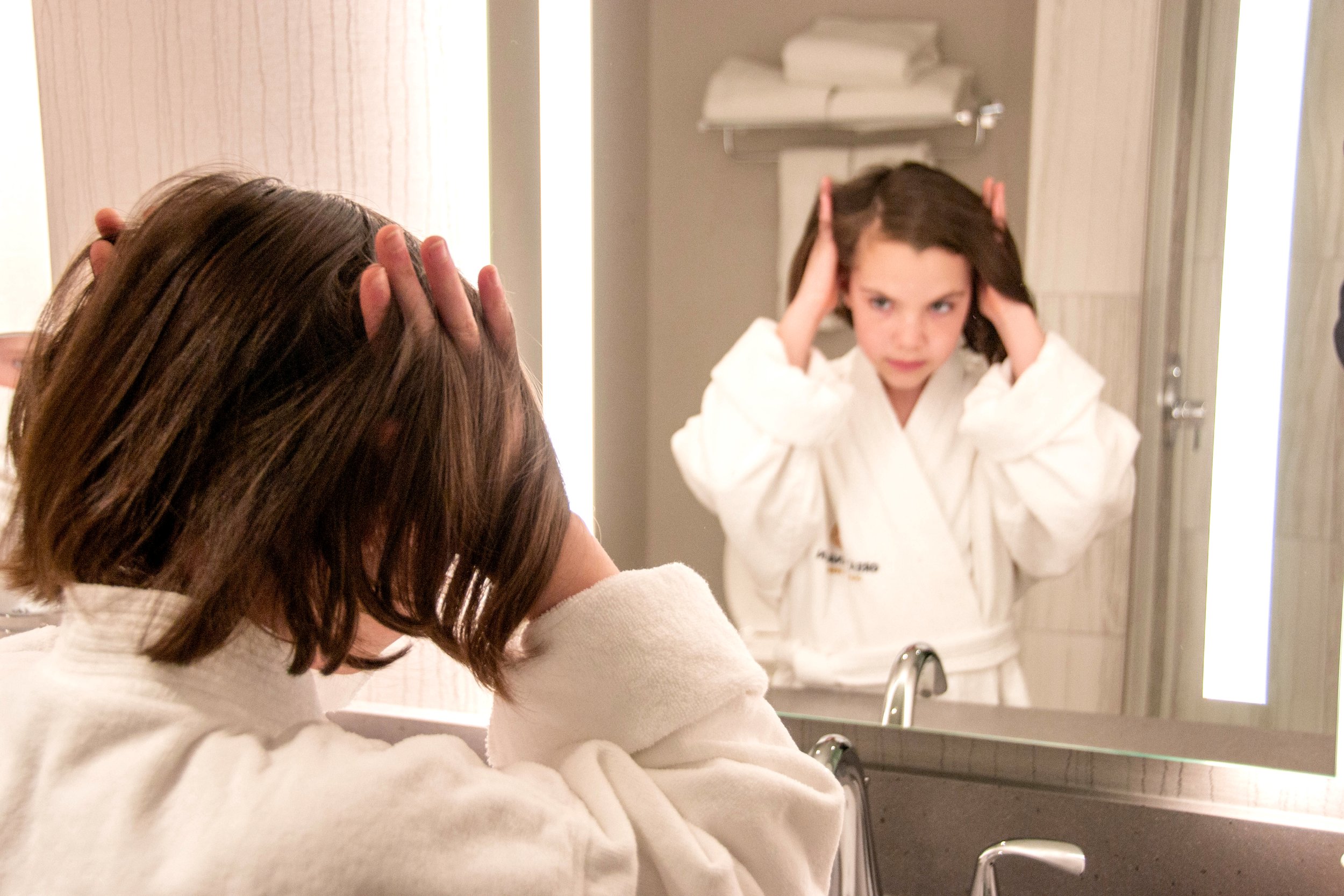 A woman in a robe scratching her scalp in the mirror, showing how to treat an itchy scalp after hair dye.