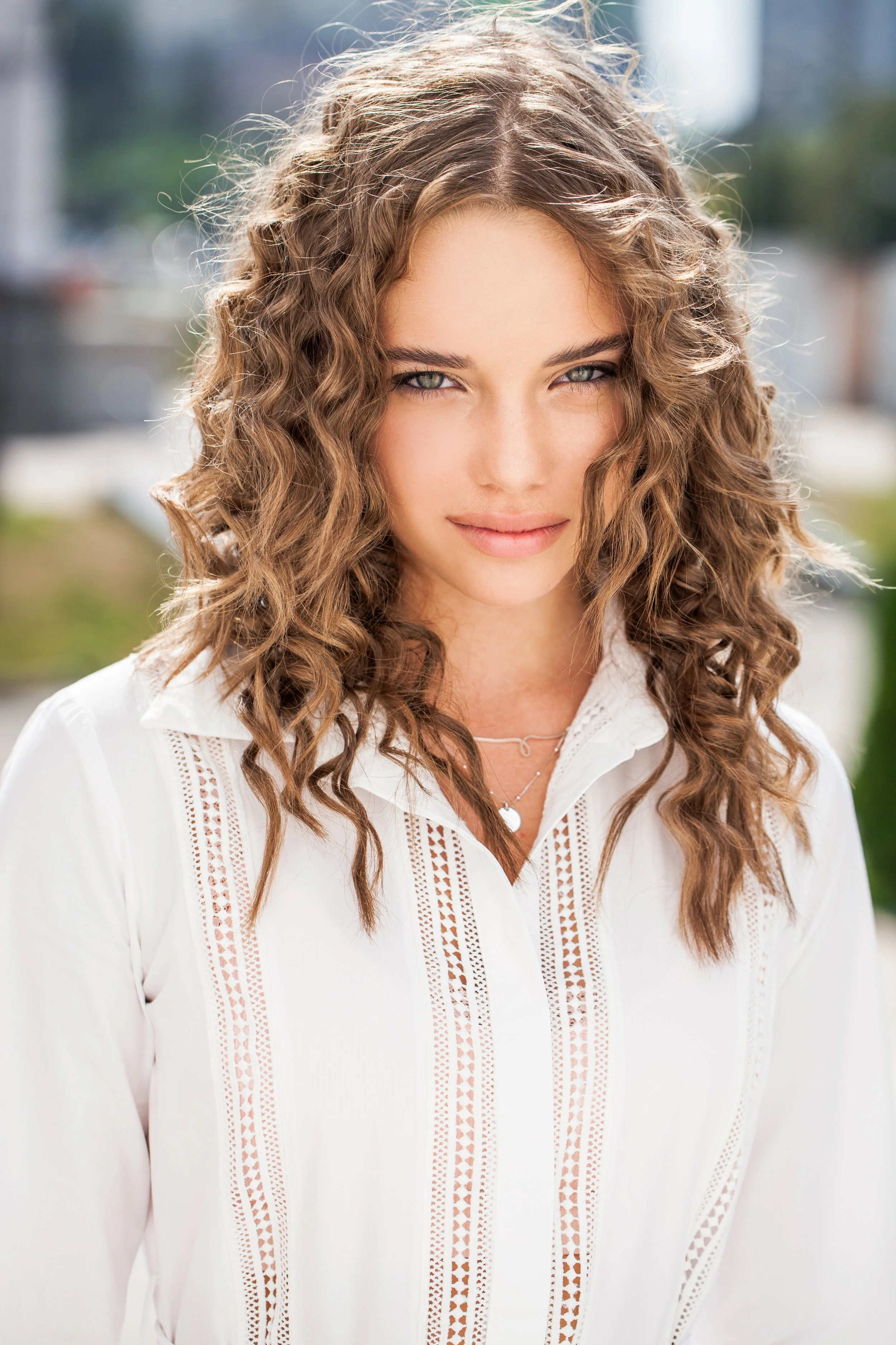 A woman with curly hair, in a woman's style, wearing a white lace blouse, smiling.