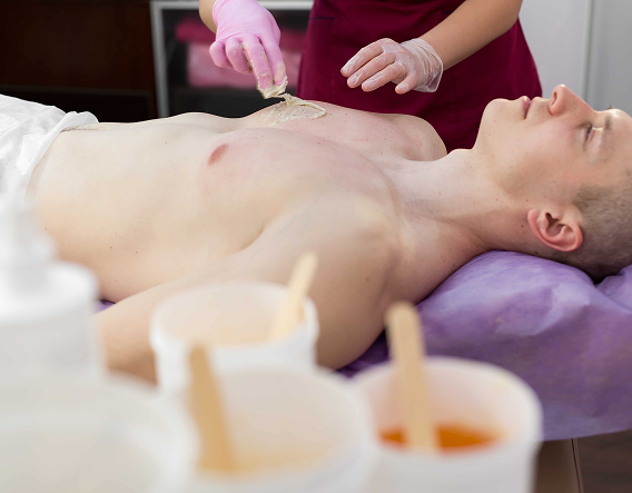Professional esthetician performing male chest waxing with warm wax during a grooming service in Buena Park