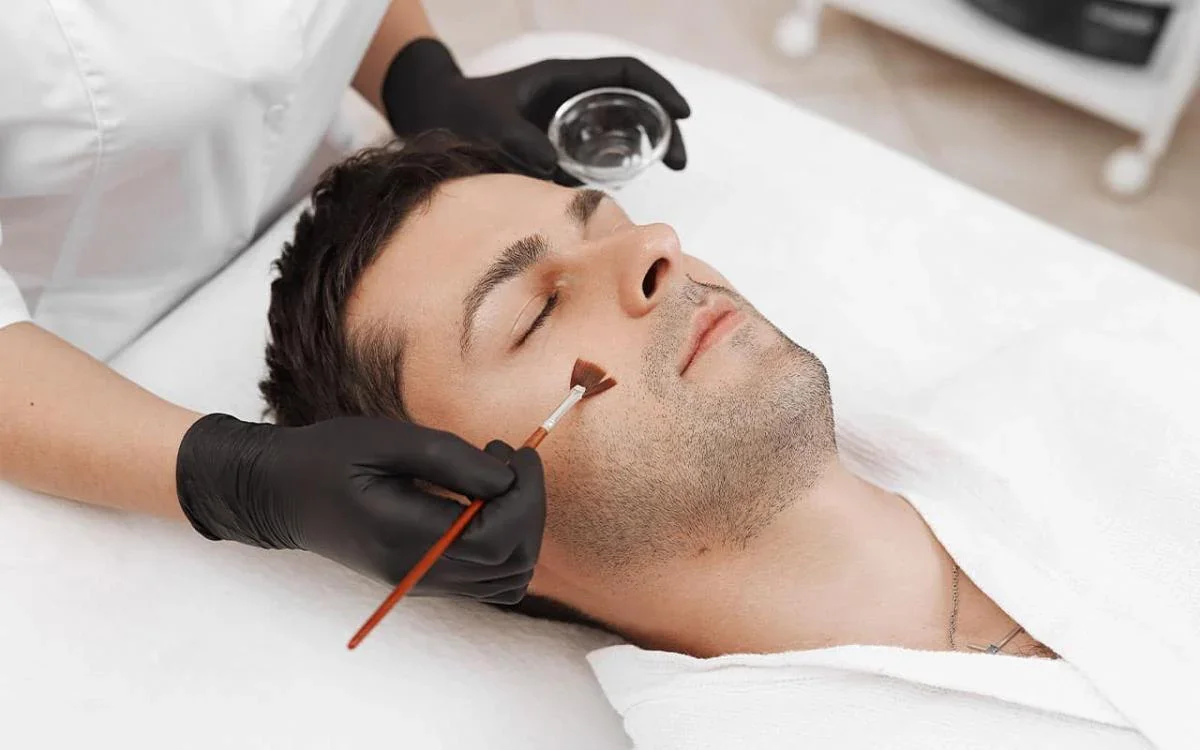 ge 2:  Esthetician applying a chemical peel treatment to a man's face.