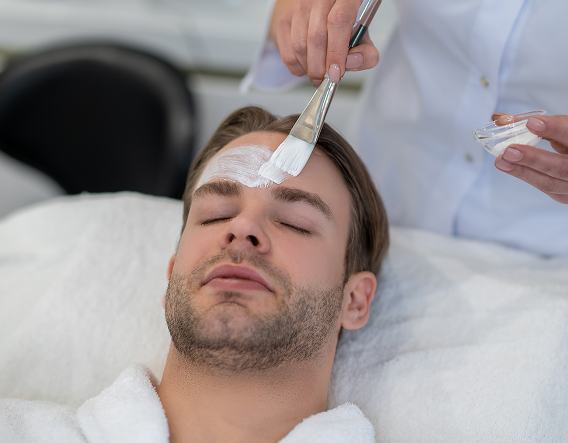 A smiling man applies an exfoliating mask, illustrating a beginner-friendly, gentle chemical peel that helps achieve clearer, healthier-looking skin.