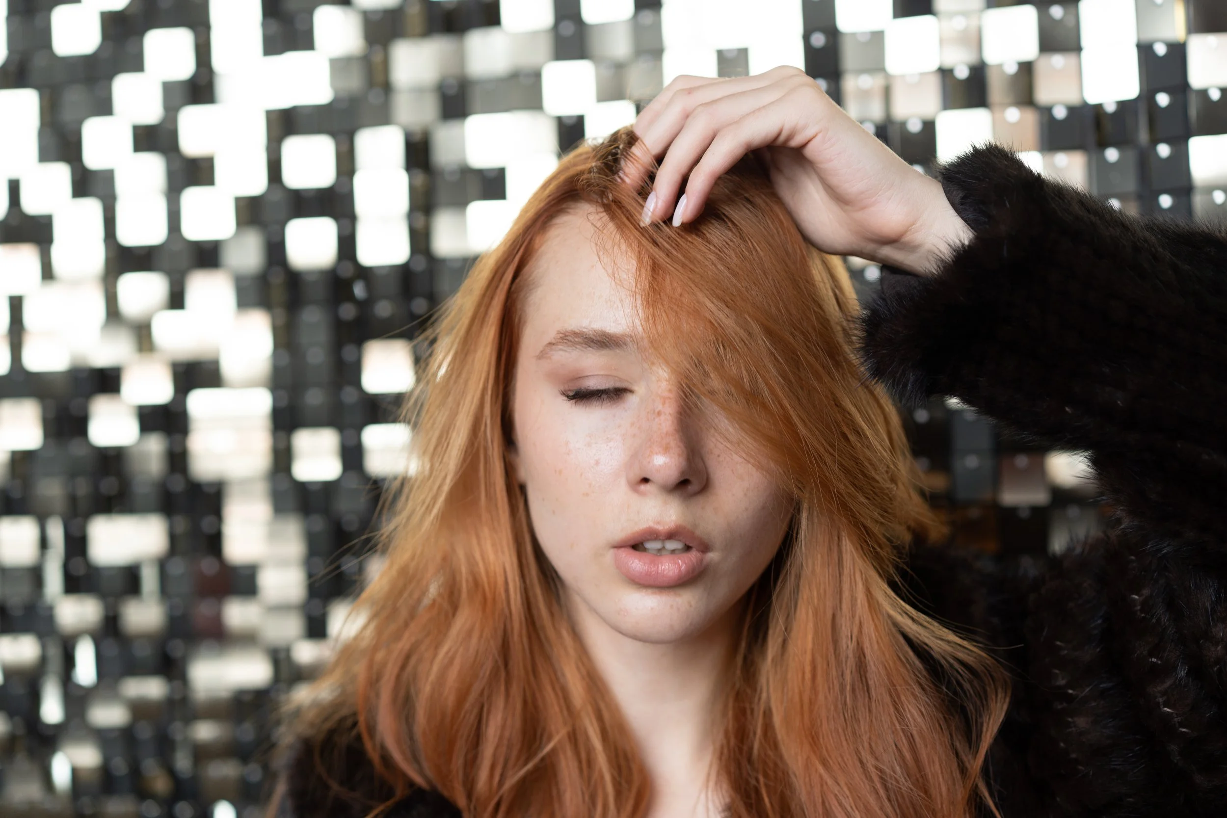 A woman with red hair lifting her hair from her forehead to inspect the scalp flaking after coloring her hair.
