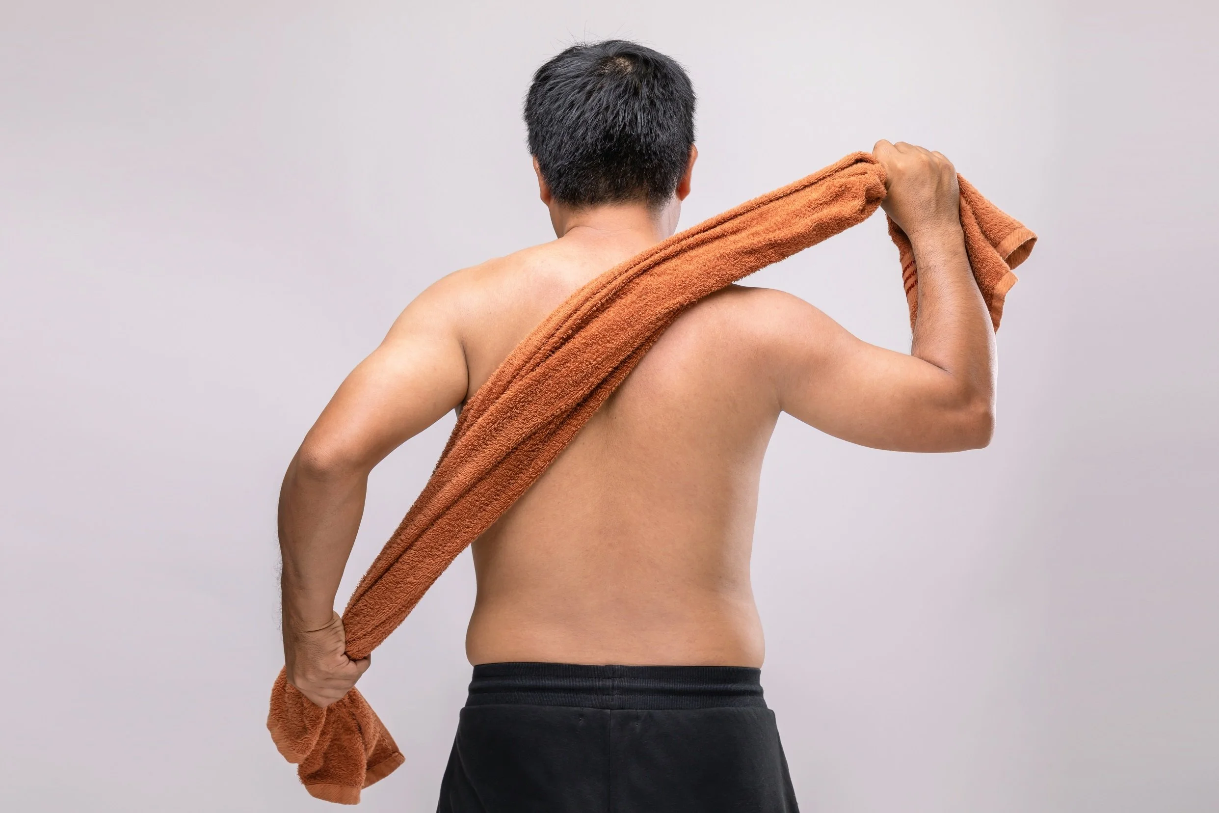 Man holding a towel and drying his back after his waxing session.