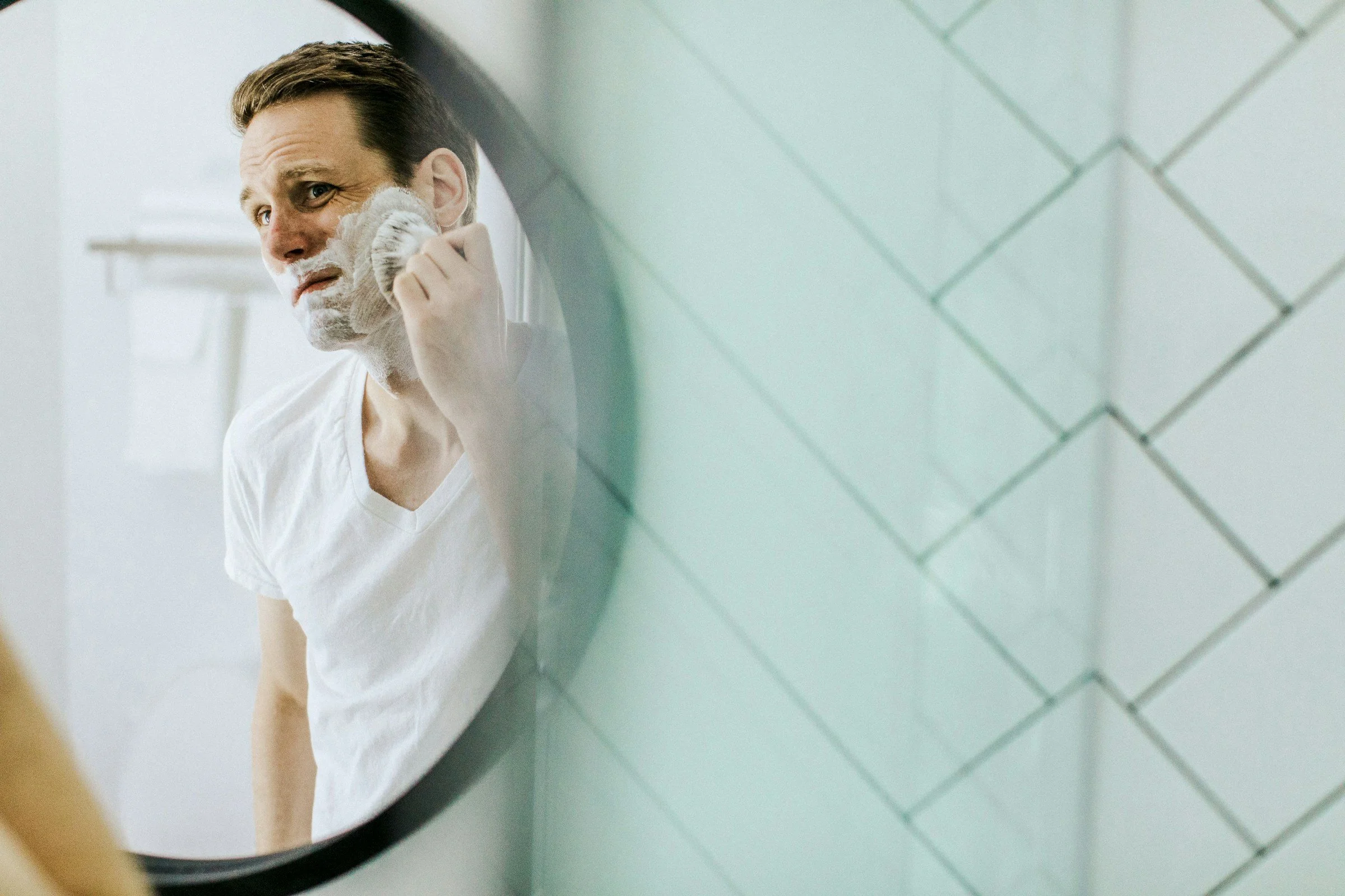 Man shaving in front of a bathroom mirror as part of a morning grooming routine.