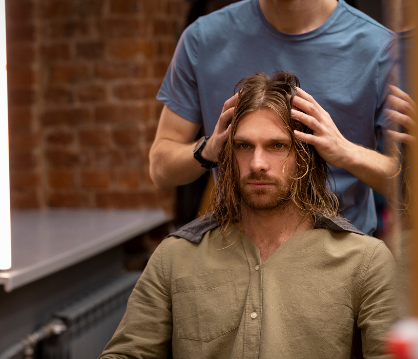 Man at home grooming in a mirror showing the easy daily styling routine that makes a men's perm cost a worthwhile investment.